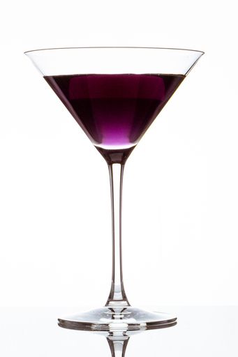 A vertical closeup of a glass of purple cocktail isolated on a white background