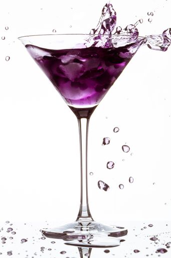 A vertical closeup of a glass of purple cocktail with splashes isolated on a white background