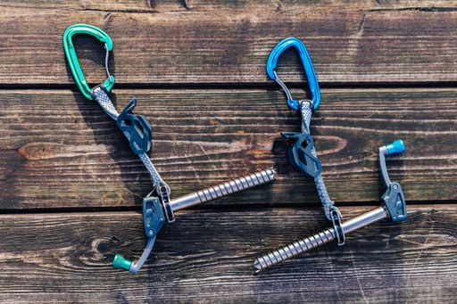 Two ice screws laying on a wooden surface. Ice climbing tools or equipment on a wooden floor. Carabiners, slings and other climbing gear.