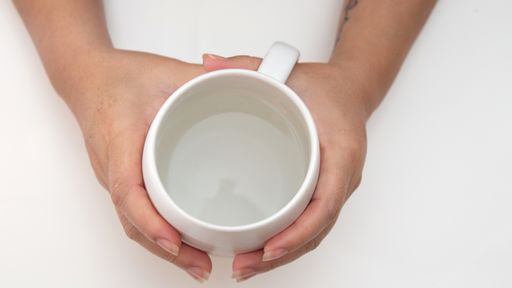 A closeup shot of a person hoding a cup of water on a white surface