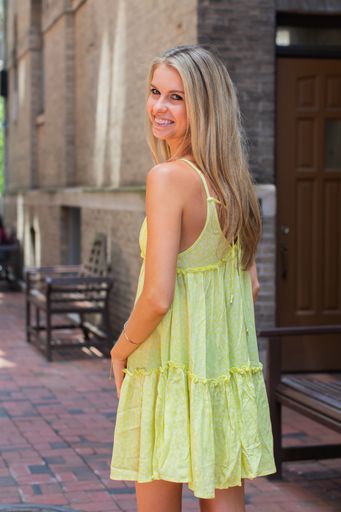 An attractive smiling blonde female in a light summer yellow dress posing in the street looking back over her shou