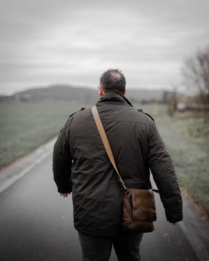 a vertical shot of an adult male with a coat and a leather bag shot from behind