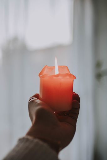 A closeup shot of a hand tightly holding a lit up candle