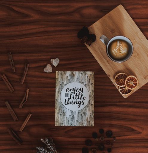 A poster put next to a cup of coffee, a small poster, dry grass and small accessories on a brown patterned table