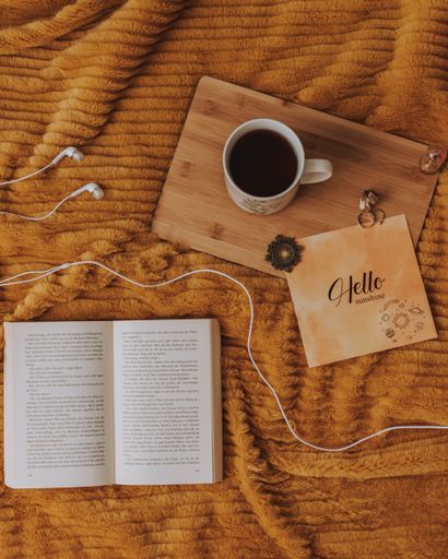 A cup of coffee, poster and a book put on a dark orange smooth surface