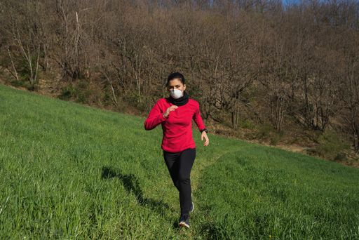 A young Caucasian female running in a park wearing a protective medical mask during Coronavirus pandemic