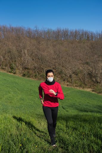 A vertical shot of a young Caucasian female running in a park wearing a protective medical mask