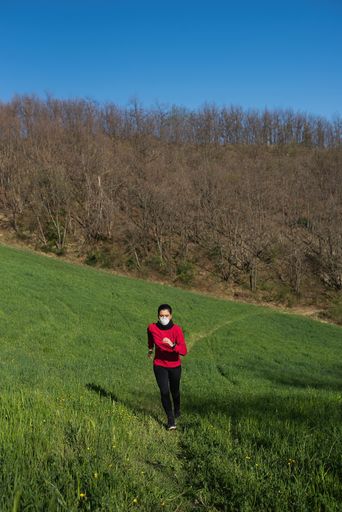 A vertical shot of a young Caucasian female running in a park wearing a protective medical mask