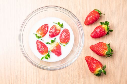 A top view of strawberries in a bowl of milk and on the table under the lights