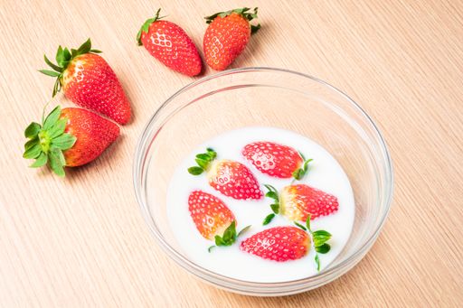 A high angle shot of strawberries in a bowl of milk and on the table under the lights