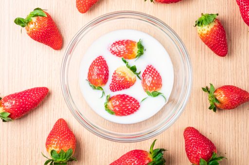 A top view of strawberries in a bowl of milk and on the table under the lights