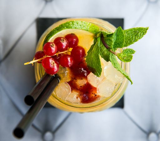 A closeupp top view of an iced cocktail with mint, lime, and currant