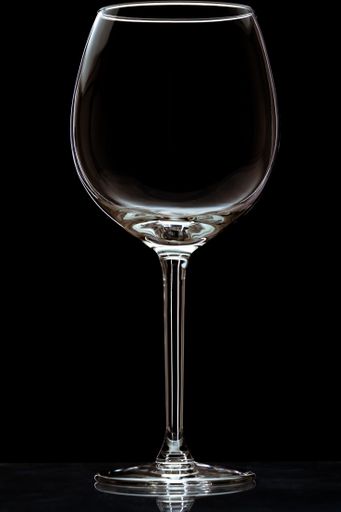 A vertical closeup of an empty wineglass on a reflective surface isolated on a black background