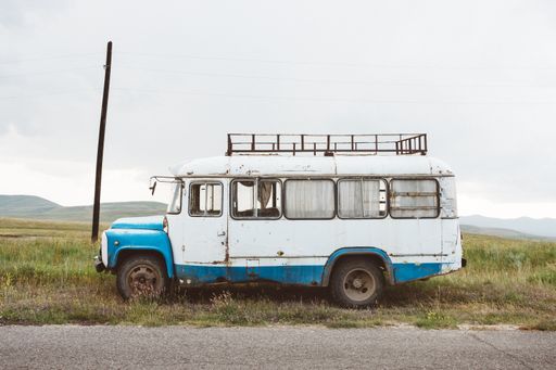 A closeup shot of an old minibus on a green landscape under a cloudy sky