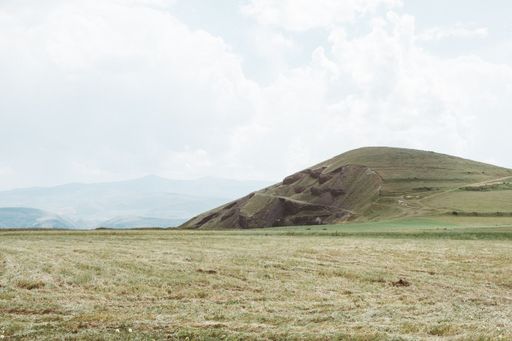 A green landscape and a mountain under a cloudy sky during daytime