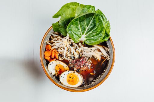 A closeup of the noodles soup in a bowl with boiled egg and  fresh vegetables