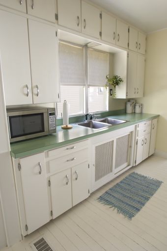 A modern kitchen with white cupboards and a green table under the lights
