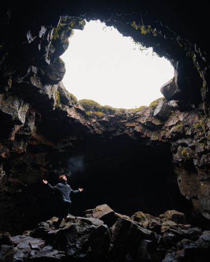 A vertical shot of a man enjoying the sunlight through the cave entra
