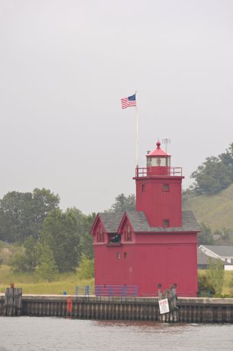 A vertical picture of The Holland Harbor Light surrounded by the water and greenery in the USA