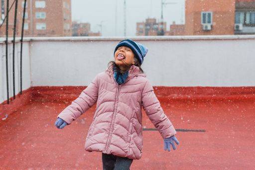 A portrait of a funny cute girl in a warm winter coat and hat catching snowflakes on her tongue