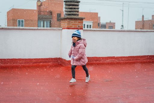 A portrait of a funny cute girl in a warm winter coat and hat catching snowflakes on her tongue
