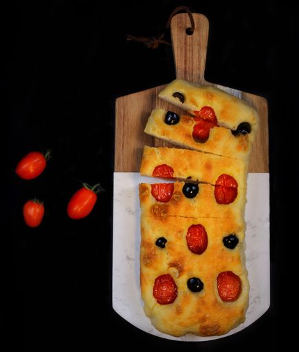 A top view of a Focaccia flat leavened oven baked Italian bread on cutting wooden board