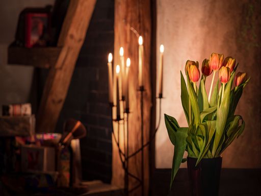An elegant ceramic vase with pink and white tulips stands in an ancient room with dimly lit candles, creating a mysterious atmosphere
