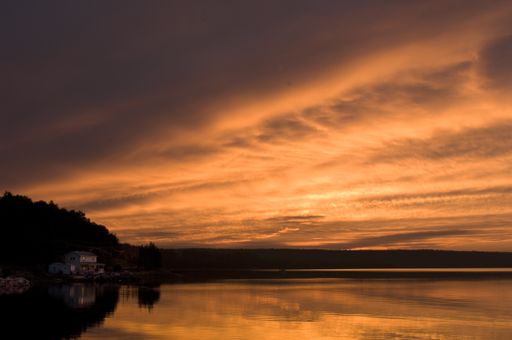 A landscape of the sea surrounded by hills under a cloudy sky during the sunset