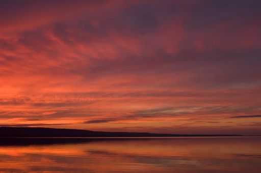 A landscape of the sea surrounded by hills under a cloudy sky during the sunset