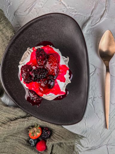 A vertical top view of ice cream with berries and syrup on a black plate
