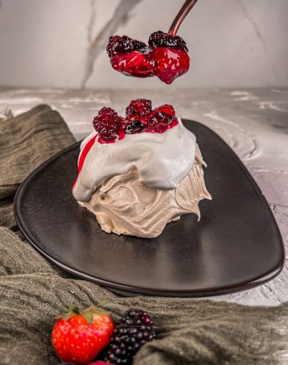 A vertical shot of ice cream with berries and syrup on a black plate