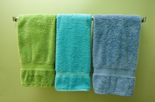 Three colourful towels on the hanger on the green wall under the lights