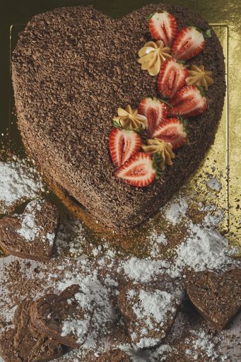 A top view of a delicious heart-shaped chocolate cake with strawberries on the table