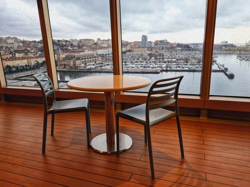 A small table with empty chairs in front of large window overlooking the city of Trieste in Italy