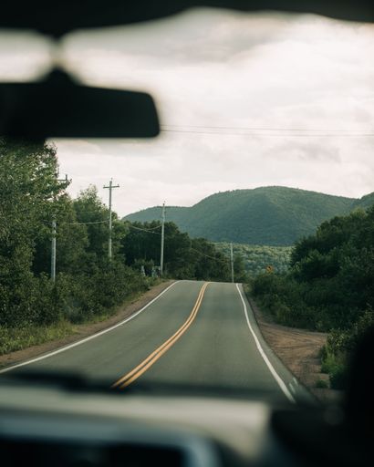 A vertical selective focus shot of long asphalt road seen behind the car windshield