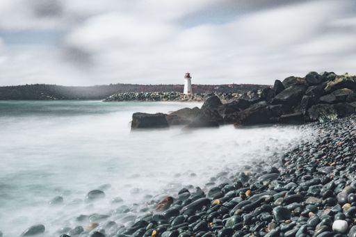 A beautiful view of a rocky shore with a broken wooden road against a lighthouse in the background