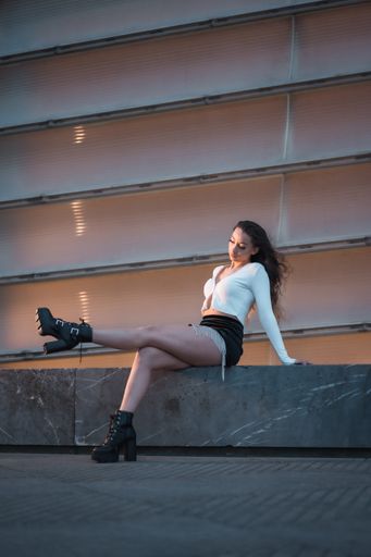 A vertical shot of a female sitting next to a grey building