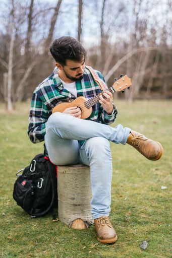 A vertical closeup of a Hispanic male playing a song on his ukulele in the woods