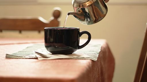 A closeup shot of black ceramic cup and a pouring tea from a teapot
