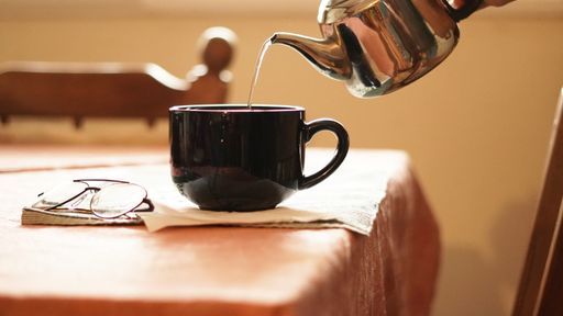 A closeup shot of black ceramic cup and a pouring tea from a teapot