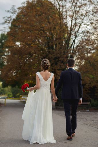 A shallow focus of a newly married couple holding hands and walking in a park