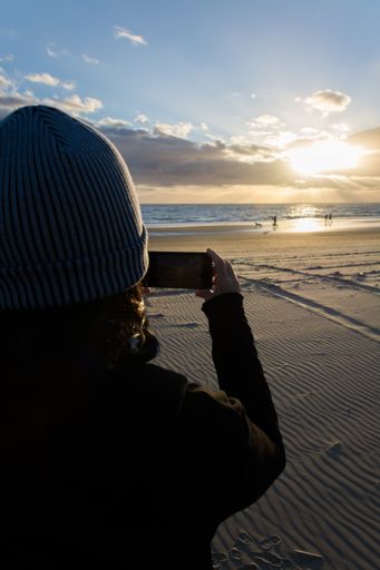 A vertical shot of silhouette of a female taking a picture of a beautiful sunrise on the beach