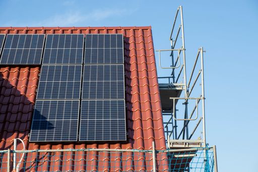A house with solar system panels on the roof under the sunlight and a blue sky