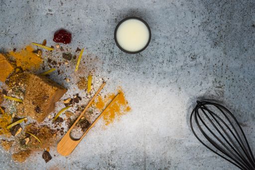 A top view of baked wholemeal sponge cake with milk, chocolate shavings, icing sugar and cinnamon on a blue granulated background