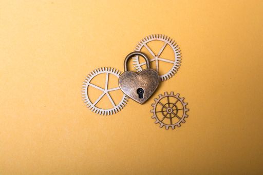 A top view of a heart shaped metal lock with wooden cogwheels on the light orange surface