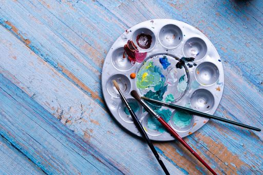 A top view of a metal painting pallet with brushes on a weathered blue wooden surface