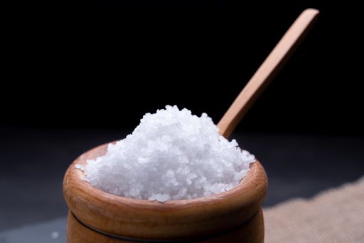 A closeup of a wooden bowl full of sea salt on a black background