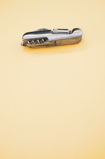 A vertical shot of a small folding pocket knife on a beige surface under the lights