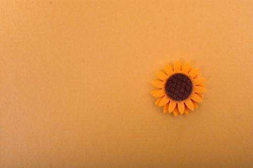 A top view of an artificial sunflower on a light brown surface - space for text