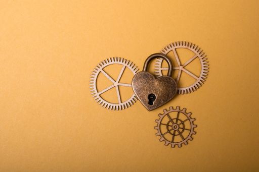 A top view of a heart shaped metal lock with wooden cogwheels on the light orange surface -